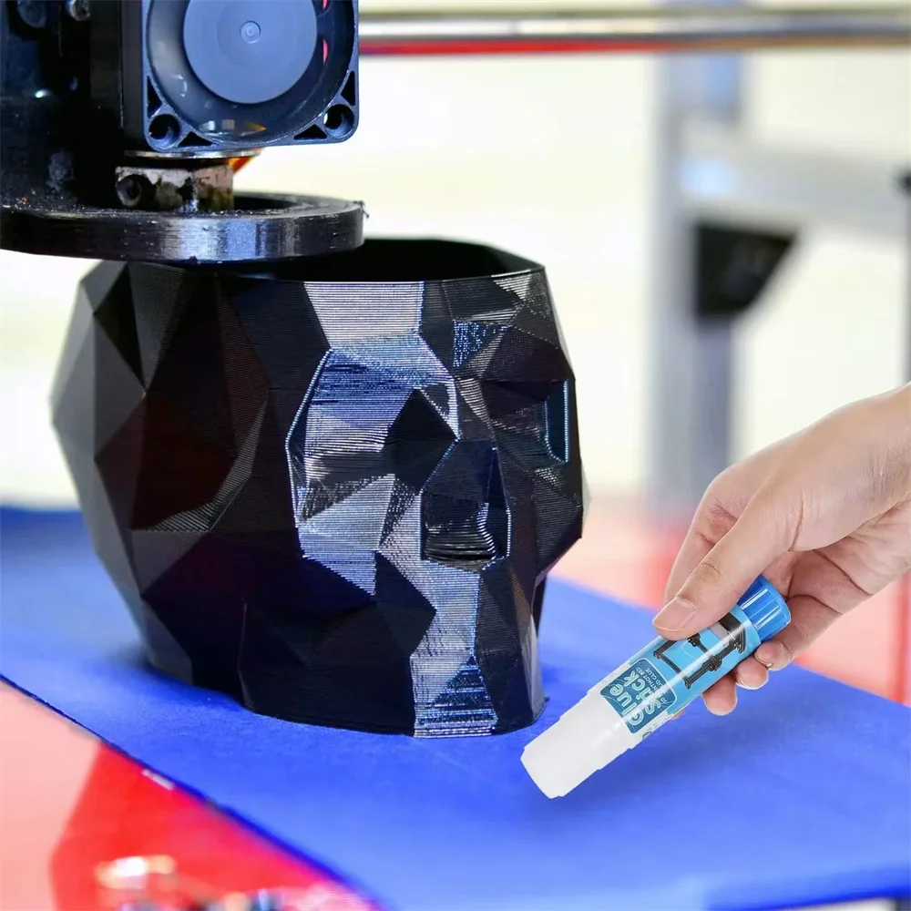 Mão aplicando uma camada fina de cola em bastão na plataforma da impressora 3D